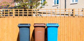 Three plastic waste bins outside a house along the fence