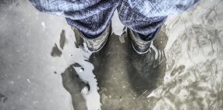 Człowiek stojący w wodzie podczas powodzi ubrany w kalosze